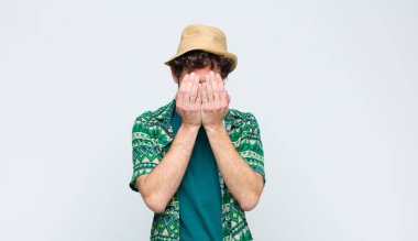 Genç turist üzgün, hayal kırıklığına uğramış, gergin ve depresif hissediyor, yüzünü iki eliyle kapatıyor, beyaz duvara karşı ağlıyor.