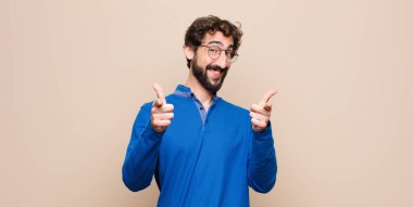 Olumlu, başarılı, mutlu bir tavırla gülümseyen genç yakışıklı kamerayı işaret ederek, elleri düz duvara dayalı silah işareti yapıyor.