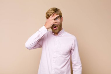 Genç sarışın adam şok olmuş, korkmuş ya da korkmuş görünüyordu. Yüzü elle kaplıydı ve parmaklarının arasından düz duvara bakıyordu.