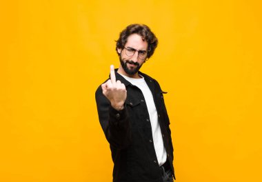 Genç çılgın yakışıklı adam kızgın, sinirli, asi ve agresif orta parmağını sallayarak turuncu duvara karşı savaşıyor.