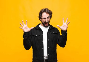 Genç çılgın yakışıklı adam panik ya da öfke içinde bağırıyor, şok olmuş, korkmuş ya da öfkeli, elleri turuncu duvara dayalı.