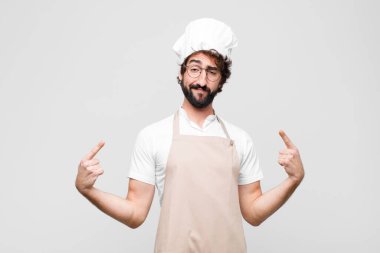 Genç çılgın şef gururlu, kibirli, mutlu, şaşırmış ve tatmin olmuş görünüyor, kendini gösteriyor, beyaz duvara karşı kazanan gibi hissediyor.