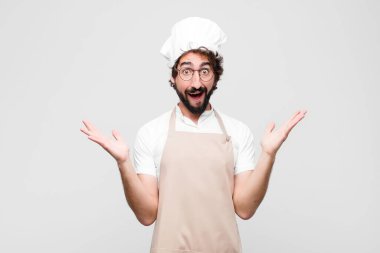 Genç çılgın şef mutlu, heyecanlı, şaşırmış ya da şok olmuş hissediyor, gülümsüyor ve beyaz duvara karşı inanılmaz bir şeye hayret ediyor.