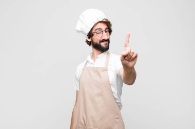 Genç çılgın şef gururla gülümsüyor ve bir numaralı pozunu başarıyla veriyor. Beyaz duvara karşı bir lider gibi hissediyor.