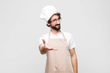 Genç, çılgın şef gülümsüyor, mutlu, kendinden emin ve arkadaş canlısı görünüyor, anlaşmaya varmak için el sıkışıyor, beyaz duvara karşı işbirliği yapıyor.
