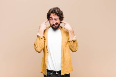 Genç çılgın adam sinirli, stresli ve sinirli görünüyor, iki kulağını da sağır edici bir ses, ses ya da yüksek sesle duvara karşı kapatıyor.