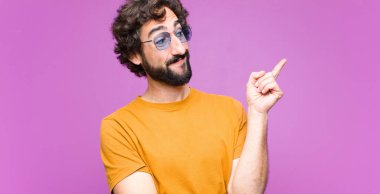 Genç çılgın adam mutlu bir şekilde gülümsüyor ve yan bakıyor, merak ediyor, düşünüyor ya da düz duvara karşı bir fikri var.