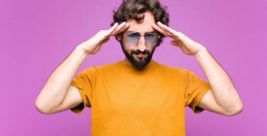 Genç çılgın havalı adam konsantre, düşünceli ve ilham verici görünüyor, beyin fırtınası yapıyor ve düz duvara karşı eller ve hayal kuruyor.