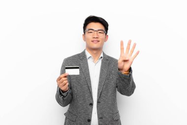 Genç Japon adam gülümsüyor ve dost canlısı görünüyor. Dört ya da dört numarayı gösteriyor. Eli önde, geri sayıyor. Kredi kartı kavramı.