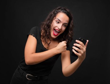 Genç, güzel bir kadın mutlu, pozitif ve başarılı hissediyor, bir meydan okumayla karşılaştığında motive oluyor veya akıllı telefon tutarak iyi sonuçları kutluyor.