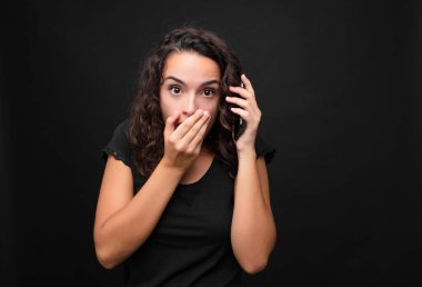 Genç ve güzel bir kadın, şok olmuş, şaşırmış bir ifadeyle ağzını kapatıyor. Sır saklıyor ya da akıllı telefon tutuyor.