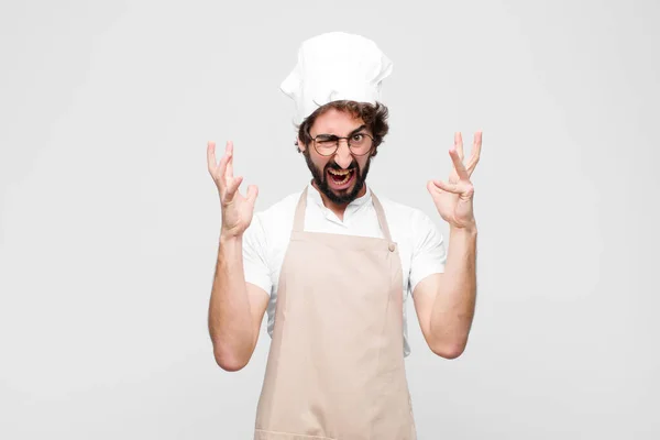 年轻的疯狂厨师高举着双手尖叫着 感到愤怒 压力和对着白墙的不安 — 图库照片