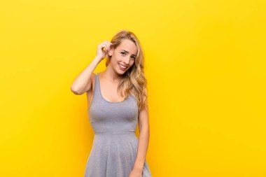 Genç sarışın kadın neşeli ve tesadüfen gülümsüyor. Turuncu duvara karşı pozitif, mutlu ve kendinden emin bir bakışla yumruk yumruğa bakıyor.