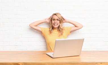 Genç sarışın kadın kendini stresli, endişeli, endişeli ya da korkmuş hissediyor. Elleri başının üstünde, dizüstü bilgisayar kullanarak hata yaptığında panikliyor.