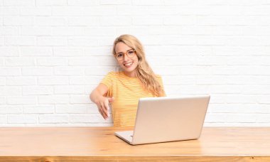 Genç sarışın kadın gülümsüyor, mutlu, kendinden emin ve arkadaş canlısı görünüyor, anlaşmayı bitirmek için el sıkışma teklif ediyor, bir dizüstü bilgisayar kullanarak işbirliği yapıyor.