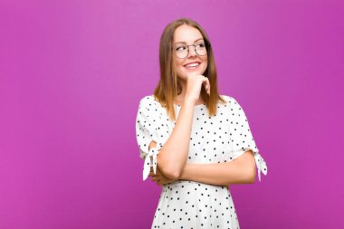 Kızıl saçlı, güzel bir kadın düşünceli, meraklı ya da hayal kuruyor, hayal kuruyor ve mor duvara karşı mekanı kopyalamak için yukarı bakıyor.