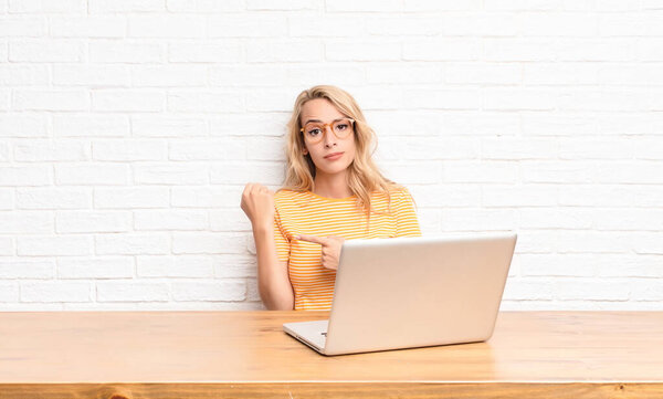 young blonde woman looking impatient and angry, pointing at watch, asking for punctuality, wants to be on time using a laptop