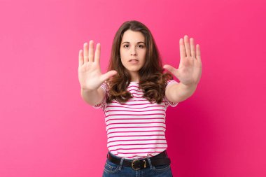 Genç ve güzel bir kadın ciddi, mutsuz, kızgın ve hoşnutsuz görünüyor. Ya da her iki avucunuzu pembe duvara dayayıp durun diyor.