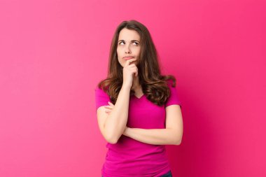 Genç, güzel bir kadın düşünüyor, kuşkulu ve şaşkın hissediyor, farklı seçeneklerle, pembe duvara karşı hangi kararı vereceğini merak ediyor.