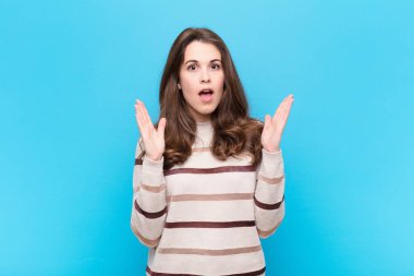 Genç, güzel bir kadın, mavi duvara karşı inanılmaz bir şey fark edince şaşırmış ve şaşırmış görünüyor.