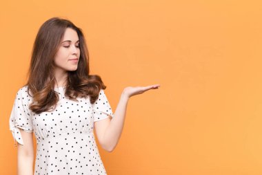 Genç, güzel bir kadın mutlu ve gülümsüyor. Turuncu duvarın karşısında duran bir nesneye ya da konsepte bakıyor.