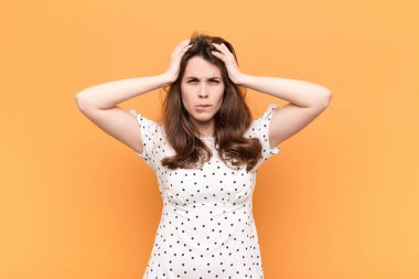 Genç ve güzel bir kadın hayal kırıklığına uğramış ve sıkılmış hissediyor, başarısızlıktan bıkmış ve bıkmış, turuncu duvara karşı sıkıcı, sıkıcı görevlerden bıkmış.