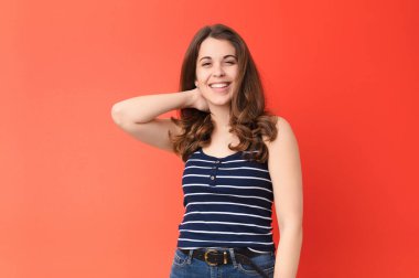 Genç ve güzel bir kadın, kırmızı duvarın karşısında neşeli ve kendinden emin bir şekilde gülüyor.