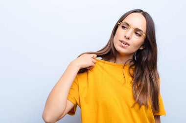 Genç, güzel bir kadın stresli, endişeli, yorgun ve hayal kırıklığına uğramış, gömleğini çekmiş, mavi duvara karşı sorunlu görünüyor.