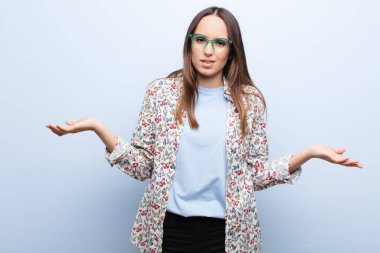 Genç ve güzel bir kadın bilgisiz ve şaşkın hissediyor, hangi seçeneği seçeceğinden emin değil, mavi duvara karşı merak içinde.