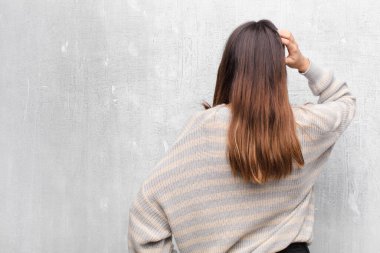 Genç, güzel bir kadın kendini cahil ve kafası karışık hissediyor, bir çözüm düşünüyor, eli kalçasında, diğeri kafasında, dikiz aynası çimento duvarında.