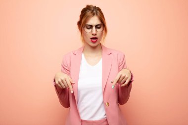 Genç, güzel, sarışın bir kadın şok olmuş, ağzı açık ve şaşırmış hissediyor. İnançsızlık ve şaşkınlık içinde aşağı bakıyor ve işaret ediyor. iş kavramı