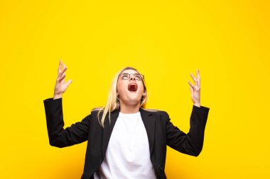 Genç, güzel sarışın kadın kendini mutlu, şaşkın, şanslı ve şaşırmış hissediyor. Zaferi kutlarken iki elini de havaya kaldırıp sarı duvara yaslanıyor.