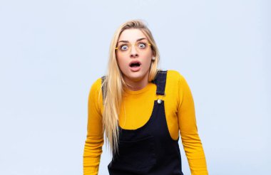 Genç, güzel, sarışın kadın dehşete kapılmış ve şok olmuş hissediyor, ağzı ardına kadar açık, düz duvara karşı şaşkınlık içinde.