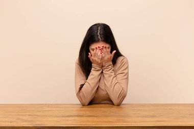 Genç, güzel bir kadın üzgün, hayal kırıklığına uğramış, gergin ve depresif, iki eliyle yüzünü kapatan, masada oturup ağlayan.