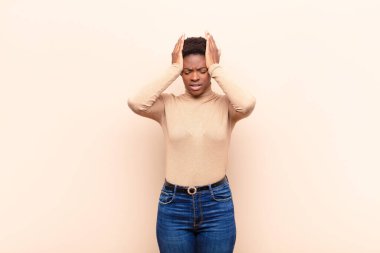 Genç ve güzel siyah kadın stresli ve endişeli, depresyonda ve hayal kırıklığına uğramış, iki elini de başa kaldırıyor.