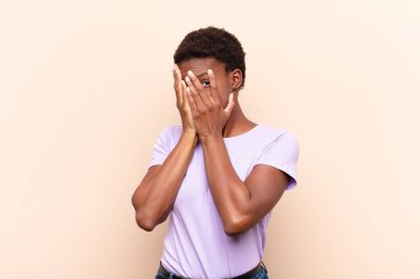 Genç, güzel, siyahi bir kadın korkmuş ya da utanmış, gözleri yarı kapalı ya da elleri kapalı gözetliyor.