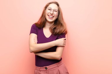 Genç sarışın kadın kollarını kavuşturup mutlu bir şekilde gülüyor, rahat, pozitif ve tatmin edici bir pozla.