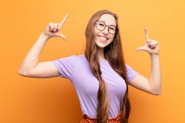 Genç sarışın kadın kendi gülüşünü çiziyor ya da özetliyor iki eliyle, pozitif ve mutlu görünüyor, sağIık kavramı.