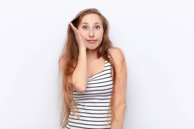 Genç sarışın kadın şok olmuş ve şaşkınlık içinde. Ağzı açık bir şekilde beyaz duvara karşı inançsızlıkla el ele tutuşuyor.