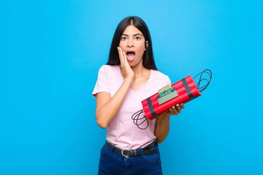 Genç, güzel, Latin bir kadın şok olmuş ve korkmuş hissediyor. Ağzı açık, elleri yanakları düz duvarda.