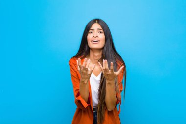 Genç ve güzel Latin kadın umutsuz ve hayal kırıklığına uğramış görünüyor, stresli, mutsuz ve sinirli, bağırıyor ve düz duvara karşı bağırıyor.