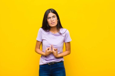 Genç, güzel, Latin bir kadın, kafası karışık ve tuhaf bir bakışla kendini işaret ediyor. Düz duvara karşı seçildiği için şaşırmış ve şaşırmış görünüyor.