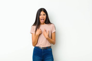 Genç, güzel, Latin bir kadın mutlu, şaşırmış ve gururlu hissediyor. Heyecanlı ve şaşırmış bir şekilde duvara bakıyor.