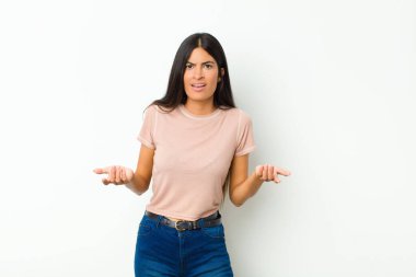 Genç, güzel, Latin bir kadın bilgisiz ve kafası karışık, hangi seçeneği seçeceğinden emin değil, düz duvara karşı merak içinde.