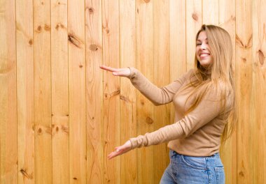 Genç sarışın kadın gülümsüyor, mutlu, pozitif ve tatmin olmuş hissediyor, fotokopi alanında nesne veya konsept tutuyor veya gösteriyor