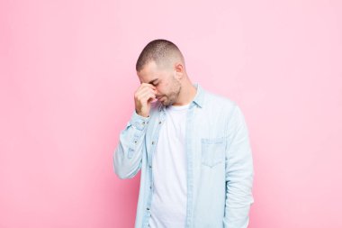 Genç yakışıklı adam stresli, mutsuz ve hayal kırıklığına uğramış, alnına dokunuyor ve düz duvara karşı şiddetli baş ağrısı çekiyor.