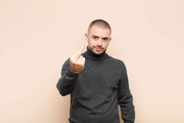 Genç, yakışıklı bir adam kızgın, sinirli, asi ve agresif orta parmağını sallayarak düz duvara karşı savaşıyor.