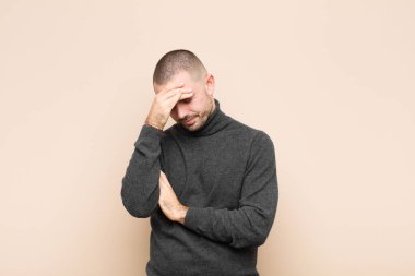 Genç ve yakışıklı bir adam stresli, utanmış ya da üzgün görünüyor. Başı ağrıyor, yüzü düz duvara yaslanmış.