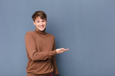 Genç sarışın adam neşeyle gülümsüyor, mutlu hissediyor ve fotokopi uzayında bir konsept gösteriyor.