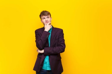 Genç sarışın adam düşünüyor, şüpheci ve şaşkın hissediyor, farklı seçenekleri var, düz duvara karşı hangi kararı vereceğimi merak ediyor.